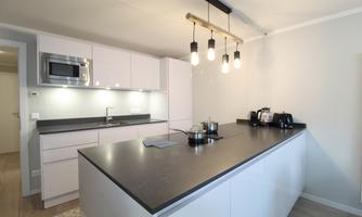 A modern kitchen with a large cooking island and elegant, white furniture. The lighting consists of cozy, hanging lamps over the island.