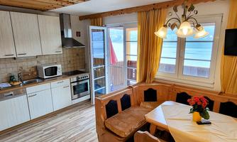 A cozy kitchen with wooden furniture and a dining table. Windows offer a view of the water and the surroundings.