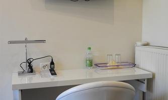 A modern workspace with a desk and a white chair. Above the table hangs a flat-screen TV, and there are water bottles on the table.