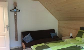 A simply furnished room with a bed and a couch. The walls are light, and there are wooden details in the room.