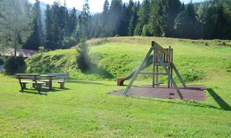 A meadow with a playground and a slide is in the foreground. In the background, there are trees and a sunny landscape.