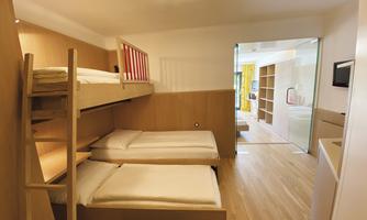 A cozy room with a bunk bed and two single beds. The room is bright and modernly furnished.