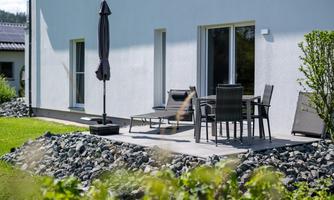 A modern terrace with a table set and lounge chairs. Surrounded by a well-maintained garden with stones and plants.