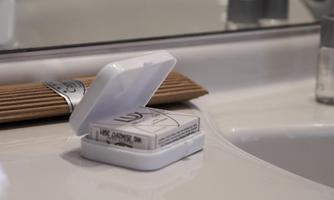 An open soap dish is on a bathroom countertop. In the background, some bathing utensils and the mirror can be seen.