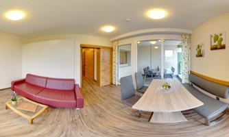 A cozy living room with a red sofa and a bright dining area. The space feels bright and inviting with modern furniture.