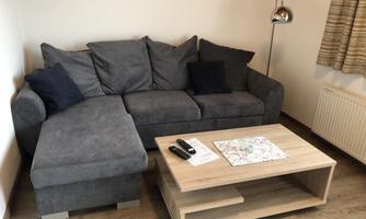 A cozy living room with a gray sofa and a wooden coffee table. Next to the table are a remote control and a small table with a card.