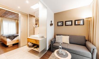 A modern room with a cozy sofa and a small table. In the background, a bed and a bathroom are visible.