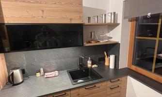 A modern kitchen with wooden cabinets and a gray work area. There is a sink and some kitchen utensils on the shelf.