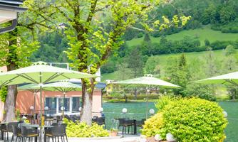 A beautiful outdoor area with tables and chairs by the water. Green foliage and sunshades create an inviting atmosphere.