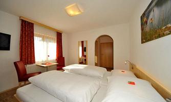A cozy hotel room with two beds and natural wooden elements. Large windows provide ample daylight and an inviting atmosphere.