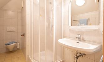 A modern bathroom with a shower cubicle, a washbasin, and a toilet. The walls are tiled with bright tiles and there is subtle lighting.