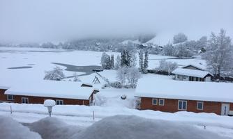 A wintry landscape with snow-covered huts and a frozen lake. The sky is gray and misty, creating a tranquil atmosphere.