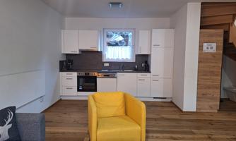 A modern kitchen with white cabinets and wooden flooring. A yellow sofa and a wooden coffee table complement the room.