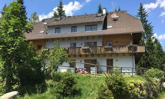 A cozy house with a balcony, surrounded by trees and greenery. The clear blue sky creates a friendly atmosphere.
