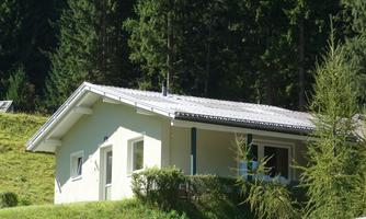 A charming house in the mountains, surrounded by green meadows and tall trees. The sun is shining, creating an inviting atmosphere.