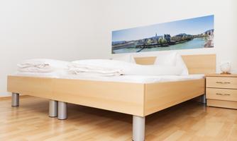 A simple bedroom with a large bed and fresh white bedding. A panoramic picture of a cityscape hangs on the wall.