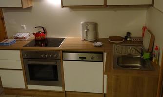 A modern kitchen with wooden surfaces and a cooking area. On the countertop, there is a red teapot and a kettle.