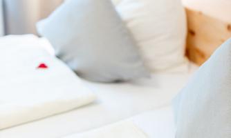 A cozy bedroom with white bedding and gray pillows. Small red hearts lie on the blankets, creating a romantic atmosphere.