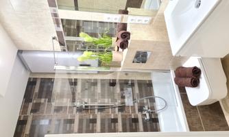 A modern bathroom with a bathtub and a shower. The walls are decorated with brown tiles, and fresh plants along with bath towels create an inviting atmosphere.