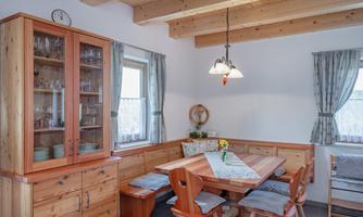 A cozy dining area with a wooden table and chairs. Wooden shelves and windows create a bright, inviting atmosphere.