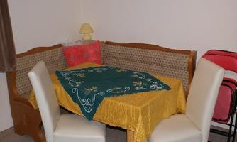 A small dining area with a cozy bench and a table. The tablecloth is yellow and decorated with green fabric.