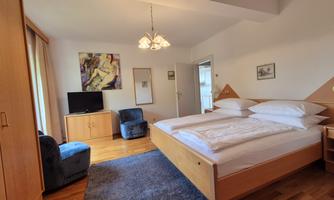 A modern room with a double bed, a television, and two blue chairs. The room is bright and tastefully designed.