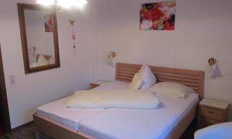 A cozy bedroom with a large double bed and modern furnishings. A colorful picture hangs on the wall, and there is a mirror as well as a pretty lamp.
