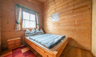 A cozy bedroom with wooden paneling and a large bed. The windows are adorned with curtains, and the floor is covered with a red carpet.