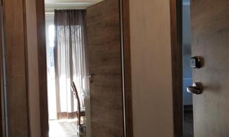 A bright hallway with wooden paneling and open doors. On the left side, there is a room with a table and chairs.