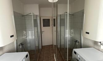 A modern laundry room with two washing machines and shower stalls. The walls are brightly tiled and reflect the equipment.