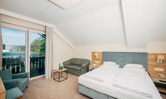 A modern room with a double bed and a cozy seating area. Large windows provide a view of the nature outside.