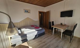 A cozy room with a double bed, a table, and two chairs. The wooden ceiling and the television give the space an inviting atmosphere.