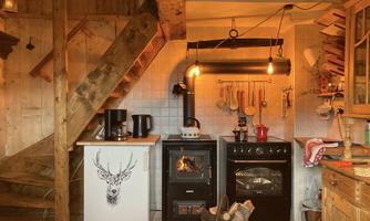 A cozy kitchen with wooden details and modern appliances. At the center is a stove with a wood oven and lovingly decorated kitchen utensils.