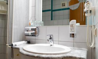 A bathroom with a round sink and a mirror. The walls are tiled, and there are towels and soap dispensers.