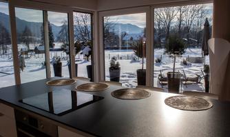 A modern kitchen with a view of snow-covered landscapes and mountains. Large windows let in a lot of light and showcase the wintry surroundings.