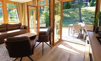 A cozy living area with large windows that let in plenty of light. Outside there is a terrace with garden furniture and a green landscape.