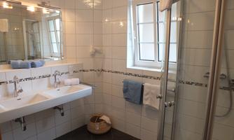 A modern bathroom with two sinks and a shower. Large windows provide plenty of daylight.