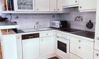 A bright, modern kitchen with white cabinets and a stylish countertop. The kitchen is equipped with appliances such as a stove, oven, and microwave.
