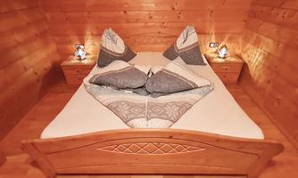 A cozy bedroom with a double bed and wood paneling. The pillows are arranged decoratively and there are nightstands with lamps.