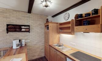 A cozy kitchen with wooden shelves and modern appliances. The walls are designed with light bricks, and a clock adds a charming touch to the space.