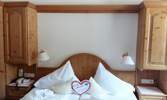 A cozy bedroom with a large bed and wood-paneled walls. On the bed lies a heart-shaped pillow.
