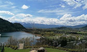 A picturesque landscape with a tranquil lake and green meadows. In the background, majestic mountains and a blue sky with white clouds can be seen.