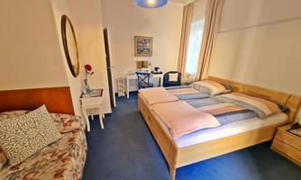 A cozy bedroom with two beds and a sofa. The room is bright and friendly, with a table and a chair.
