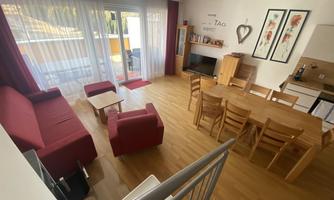 A modern living room with a red sofa and a wooden dining area.  
Large windows provide plenty of daylight.