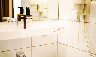 The bathroom in the Small Room impresses with its compact and practical features. Bright tiles, a sink with a mirror, and an integrated hairdryer provide everything necessary for the stay. Toiletries and storage spaces ensure additional comfort in a classic, unrenovated atmosphere.