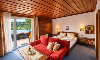 A cozy room with a red couch and a large window that offers a view of nature. The wood paneling and warm colors create a relaxed atmosphere.
