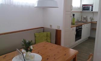 A bright kitchen with a wooden table and a cozy bench. The modern amenities include a stove, a microwave, and decorative elements.