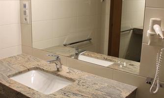 A modern bathroom with an elegant stone sink. There is a large mirror and bright lighting on the wall.