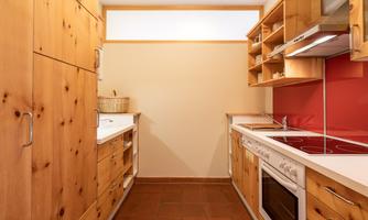 A modern kitchen with wooden cabinets and red walls. The amenities include a stove, a refrigerator, and ample storage space.
