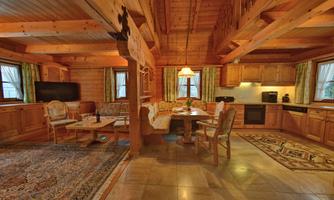 A cozy living space with wooden paneling and a large dining table. The kitchen is modernly furnished and the room has large windows with a view outside.
